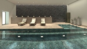 Un espace piscine intérieur moderne, avec un mur en pierre, trois chaises longues et une piscine à fond de verre.