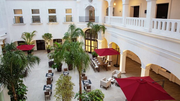 Une vaste cour intérieure, dotée de plusieurs espaces de restauration, de palmiers et de parasols rouges.