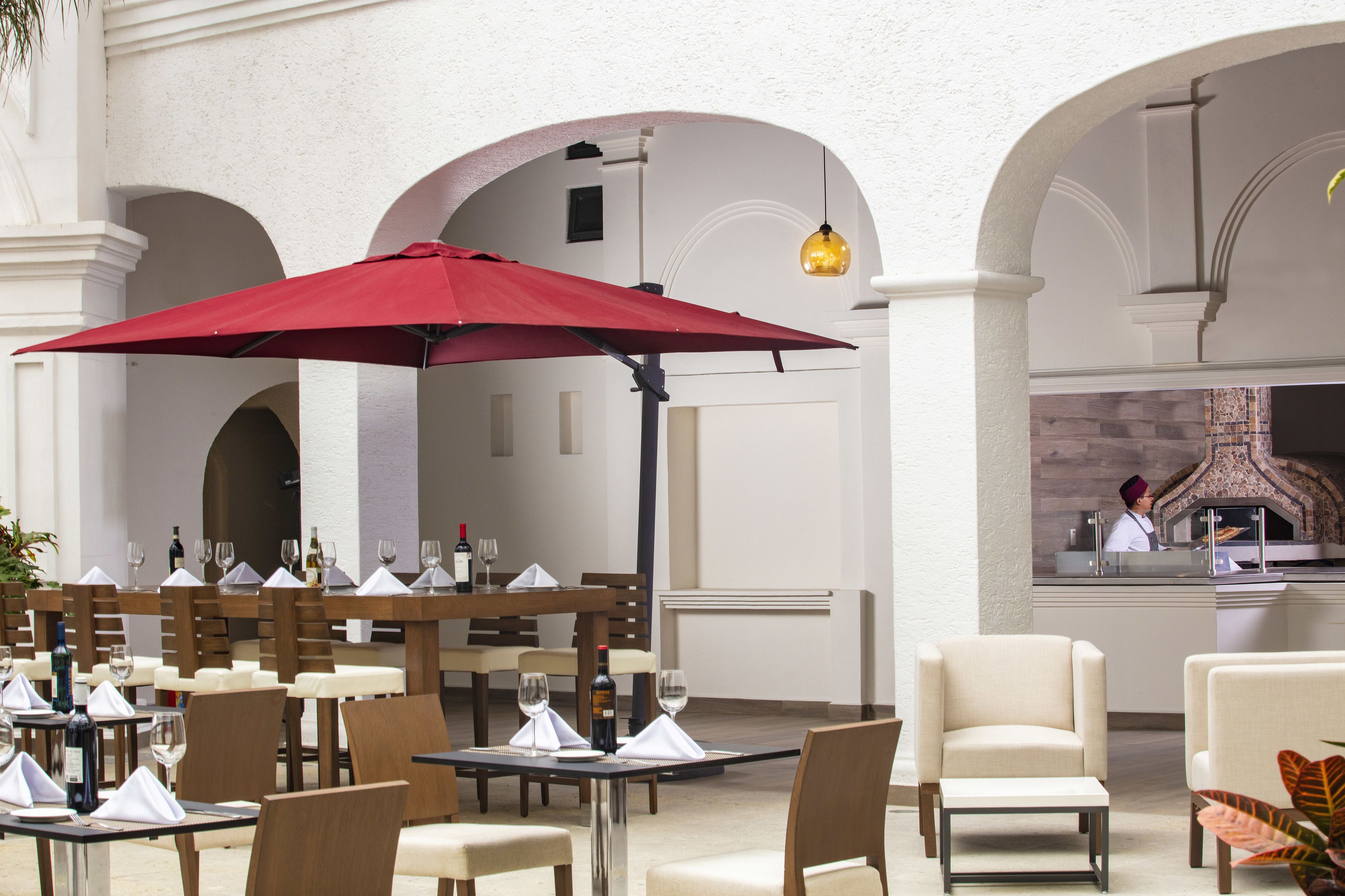 An outdoor dining area with tables, chairs, and a red umbrella.