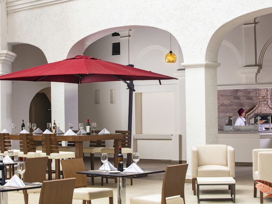 Un área de comedor al aire libre con mesas, sillas y un paraguas rojo.