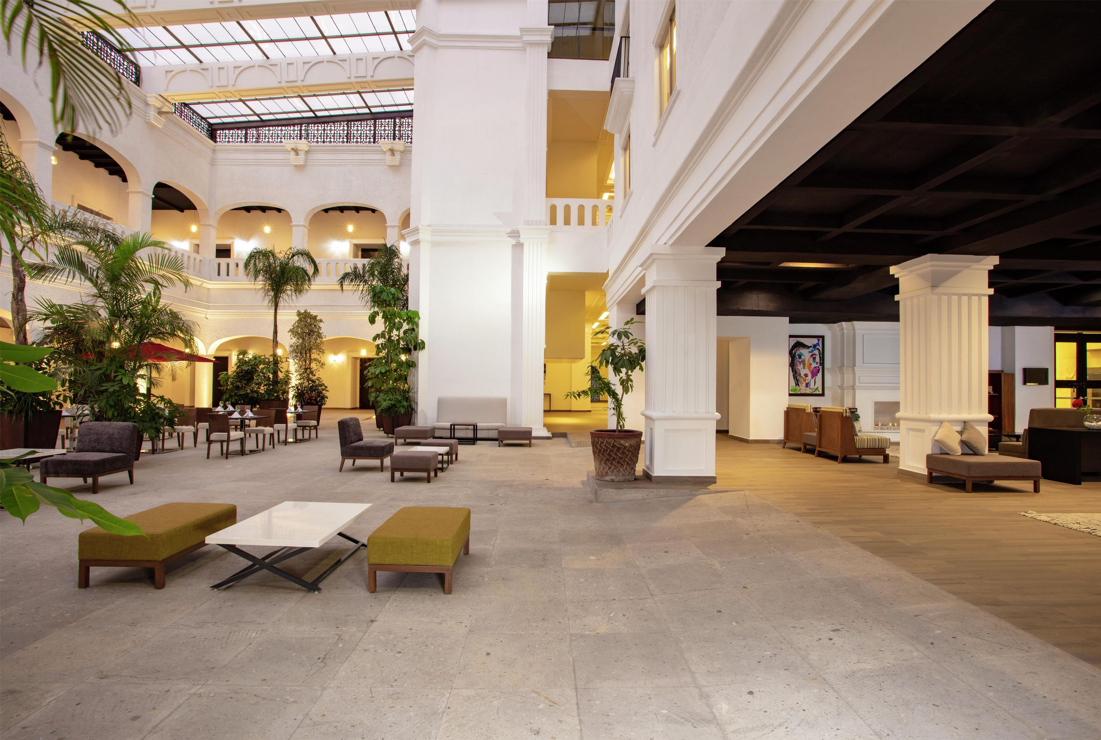 A spacious lobby with multiple seating areas, a glass ceiling, and indoor plants.