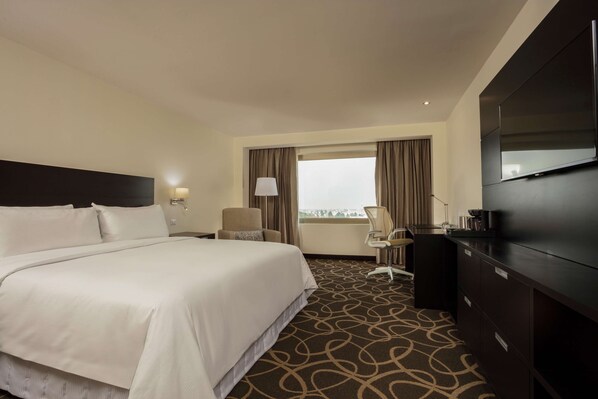 Een hotelkamer met een groot bed, een bureau, een stoel, een televisie en een raam met gordijnen.