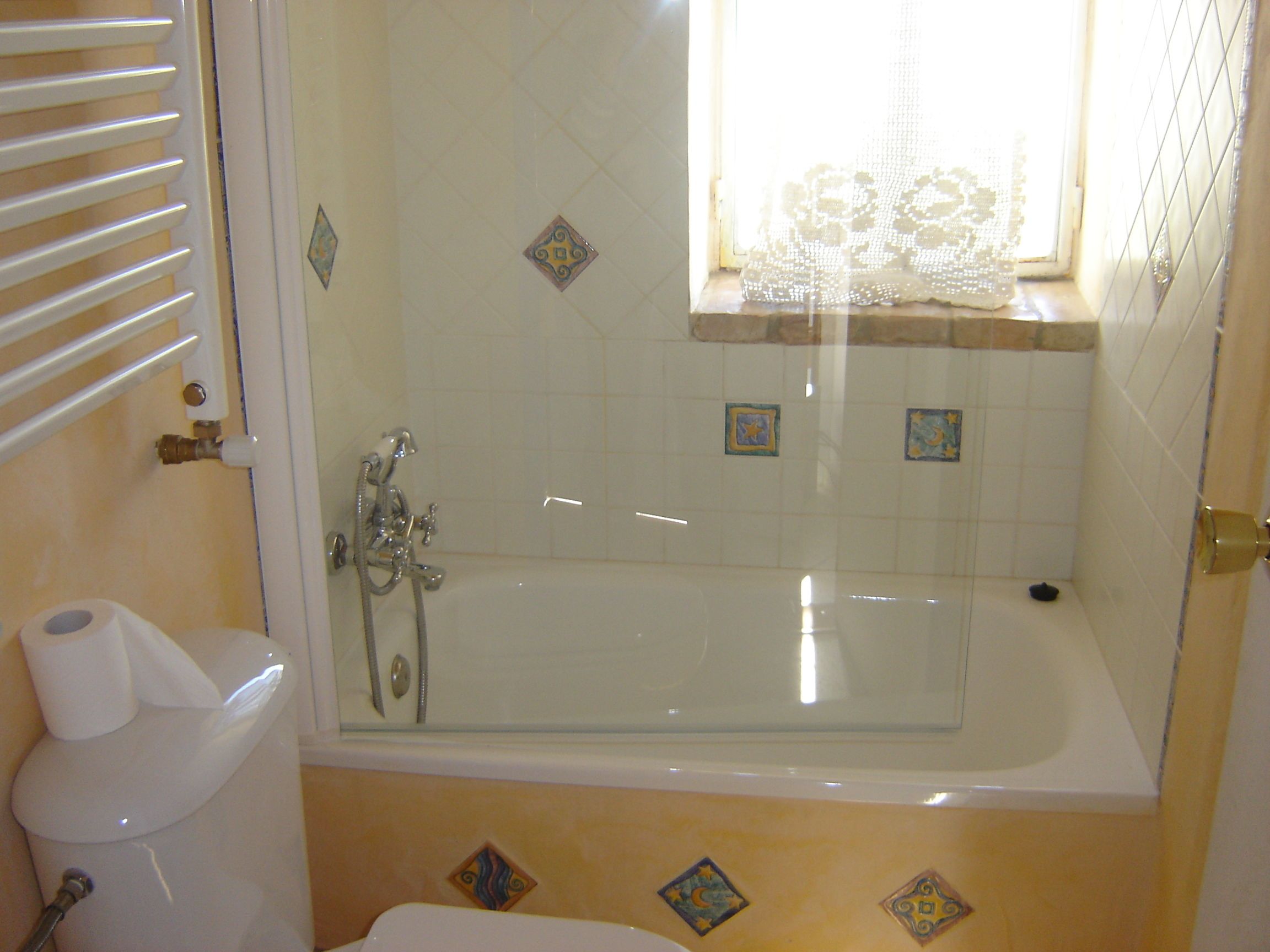 Un baño con bañera empotrada en cristal, inodoro y ventana con azulejos decorativos.