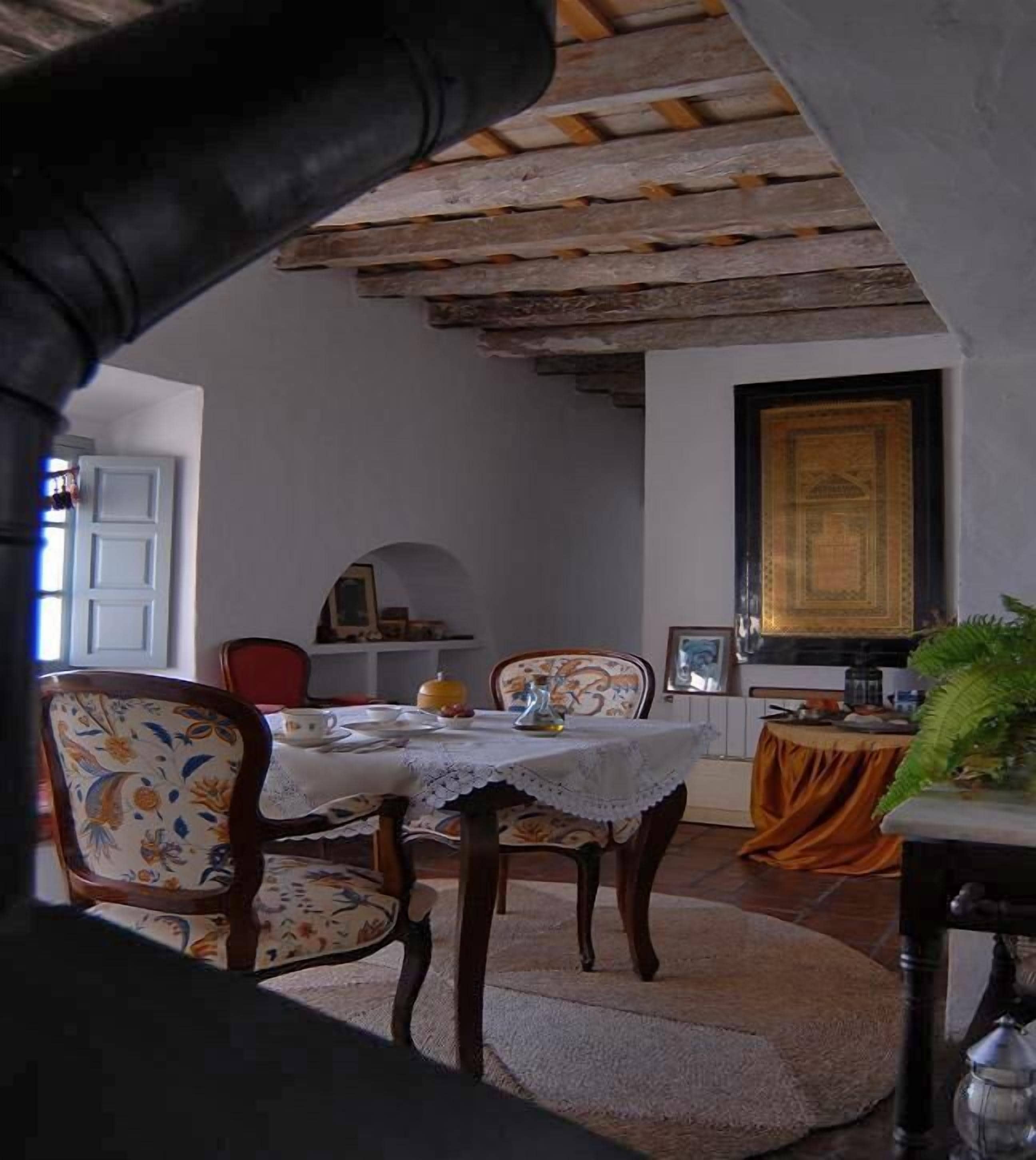 A dining area with wooden beams, floral-patterned chairs, a table set with plates, cups, and a teapot.