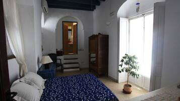 A bedroom with a bed, a desk, a chair, a wardrobe, a potted plant, and a staircase leading to an upper level.