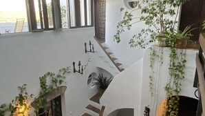 A spacious interior with a central staircase, multiple windows, and various potted plants. - La Casa de Bovedas (Arcos de la Frontera)