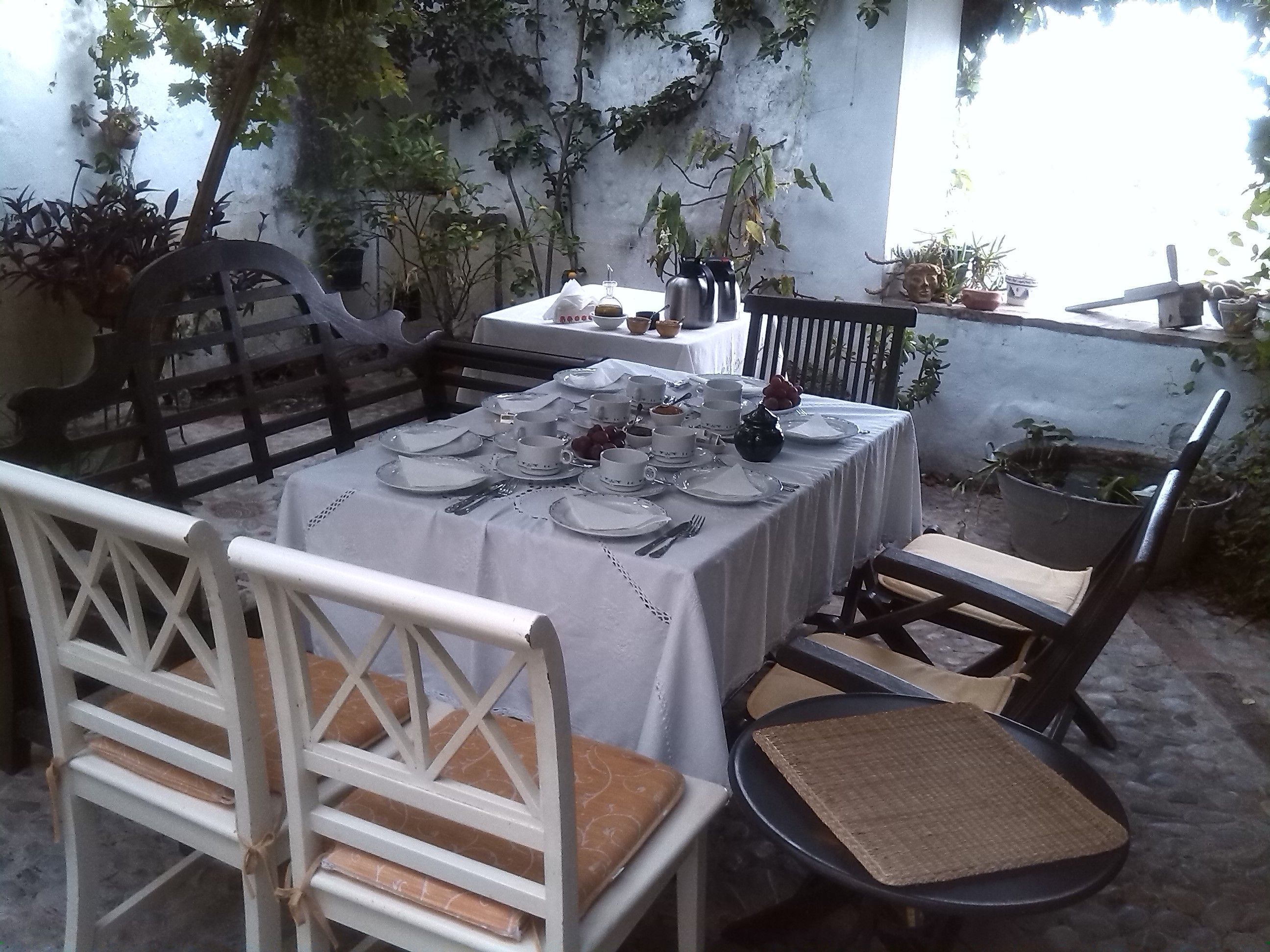 An outdoor dining area with a table set for four, surrounded by chairs, and a small round table with a mat.