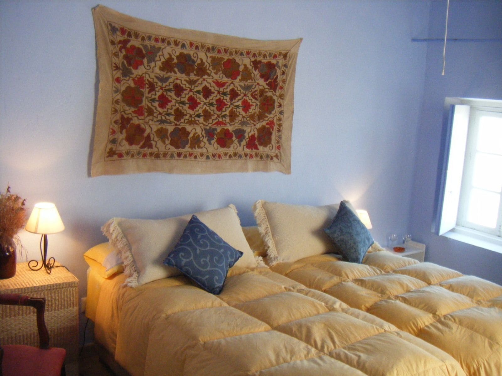Une chambre à coucher avec un lit, des oreillers, une lampe et une tapisserie au mur.