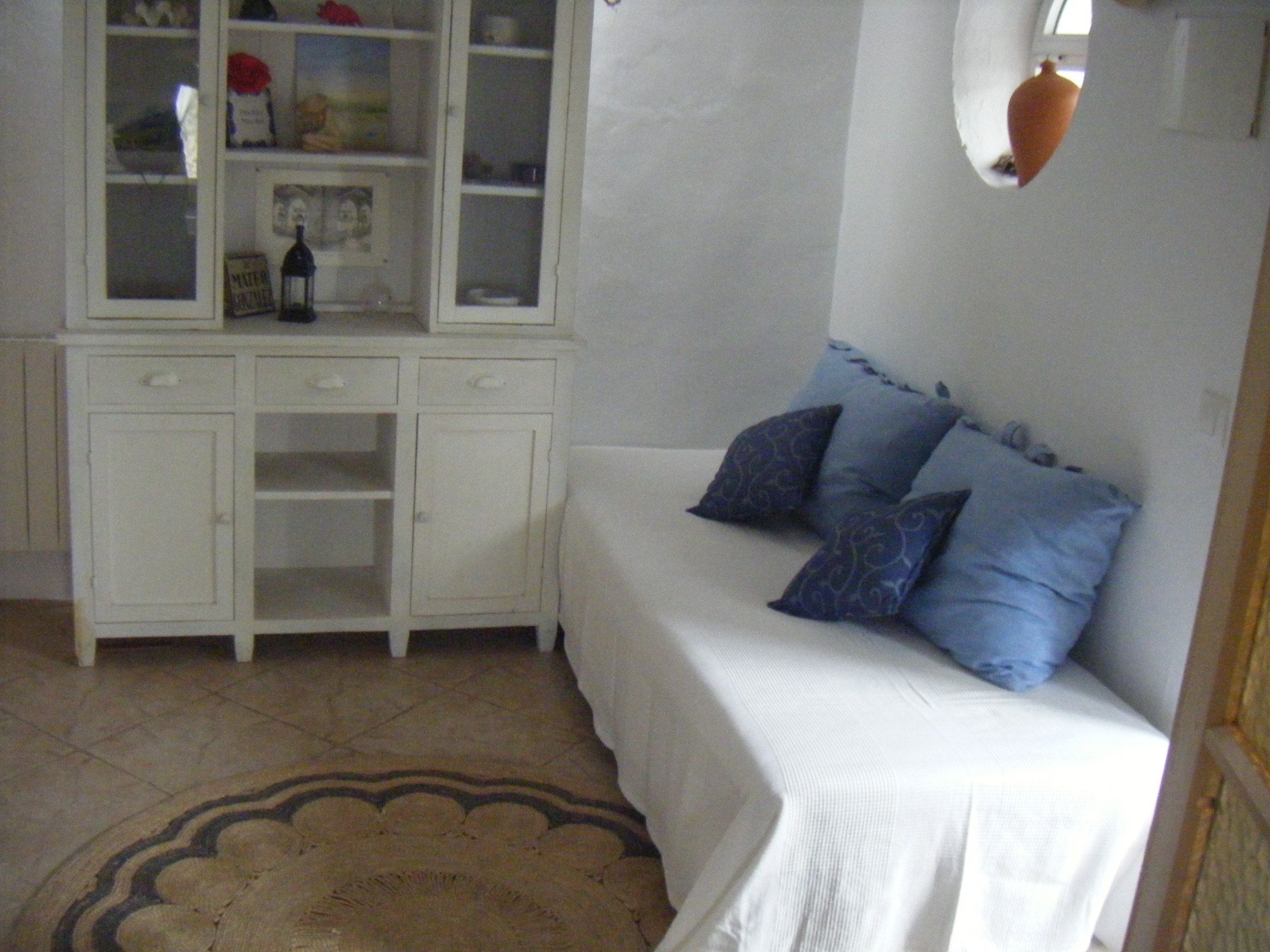 Een slaapkamer met een wit bed, blauwe kussens, een witte kast met glazen deuren en een kamerbreed tapijt met een patroon.