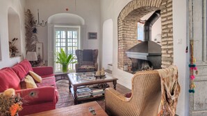 A cozy living room with a fireplace, a red sofa, a wicker chair, and a coffee table. - La Casa de Bovedas (Arcos de la Frontera)