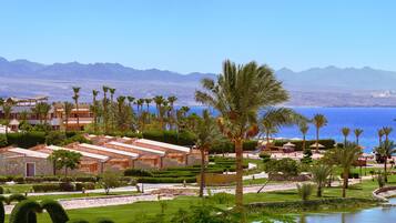 Un resort con varias construcciones, palmeras y vistas al mar y las montañas.