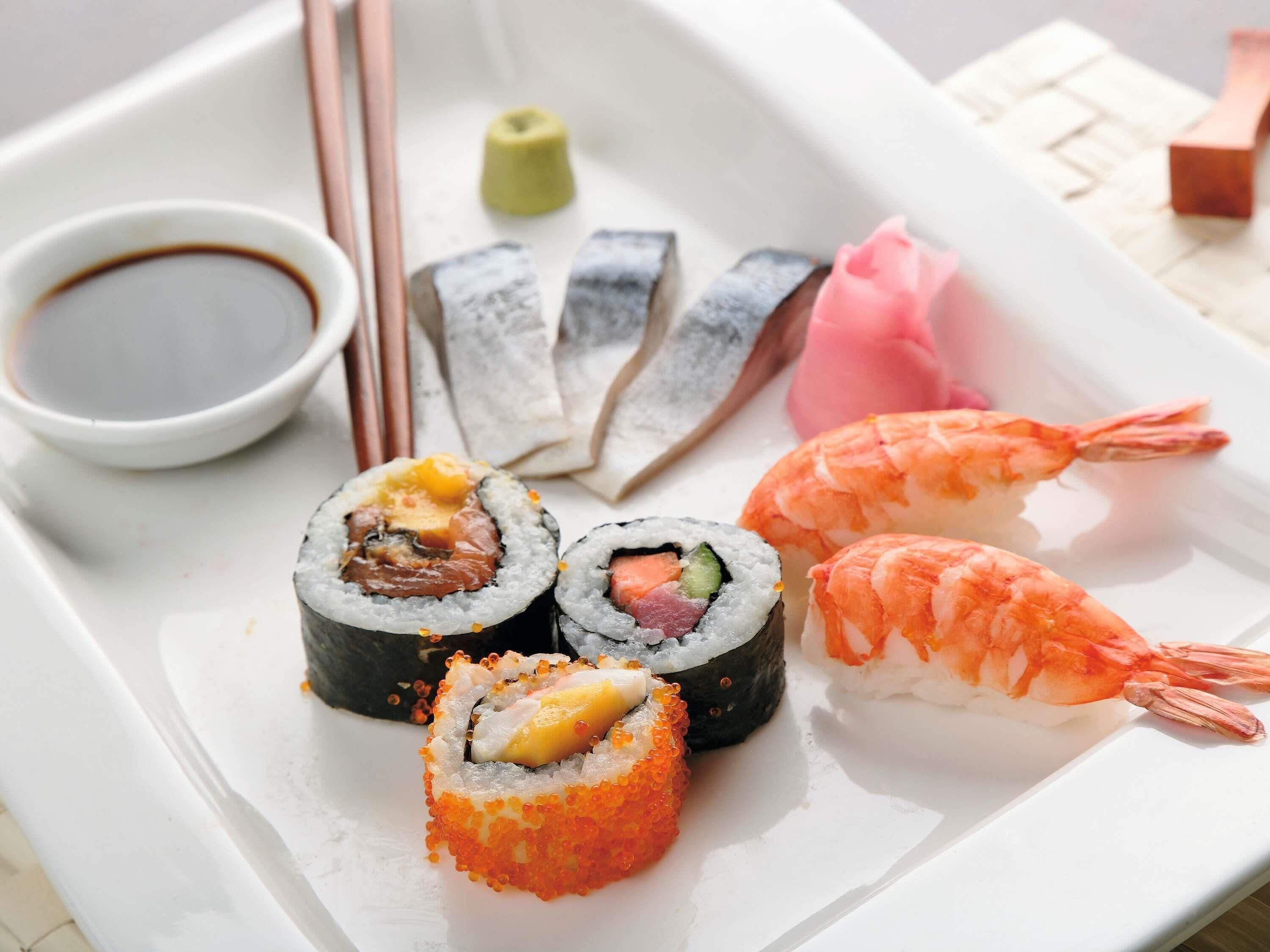 Ett fat med olika sorters sushi, inklusive nigiri och sashimi, en liten skål med sojasås och ett par ätpinnar.