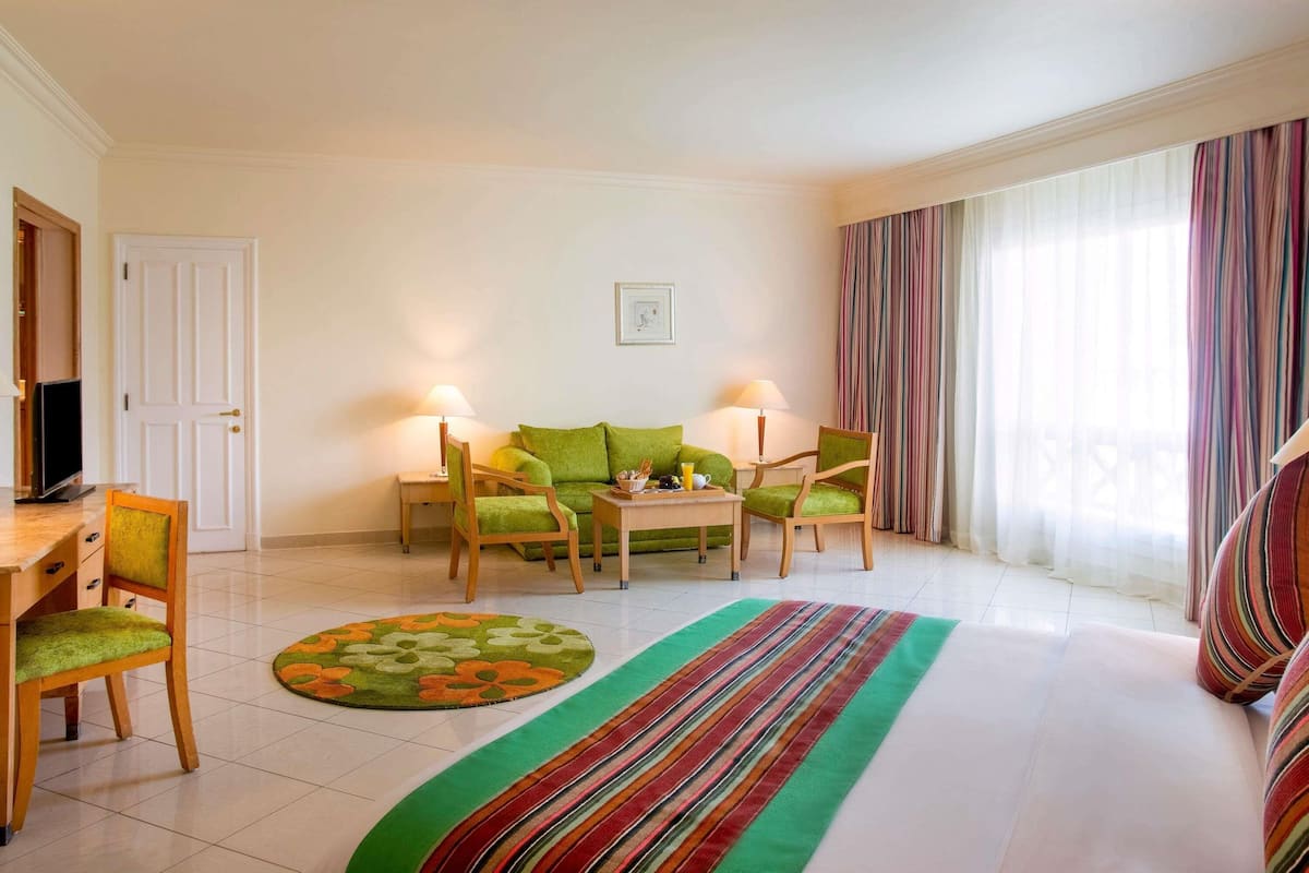 A room with a bed, a desk with a chair, a sofa, two lamps, a television, and a window with curtains.