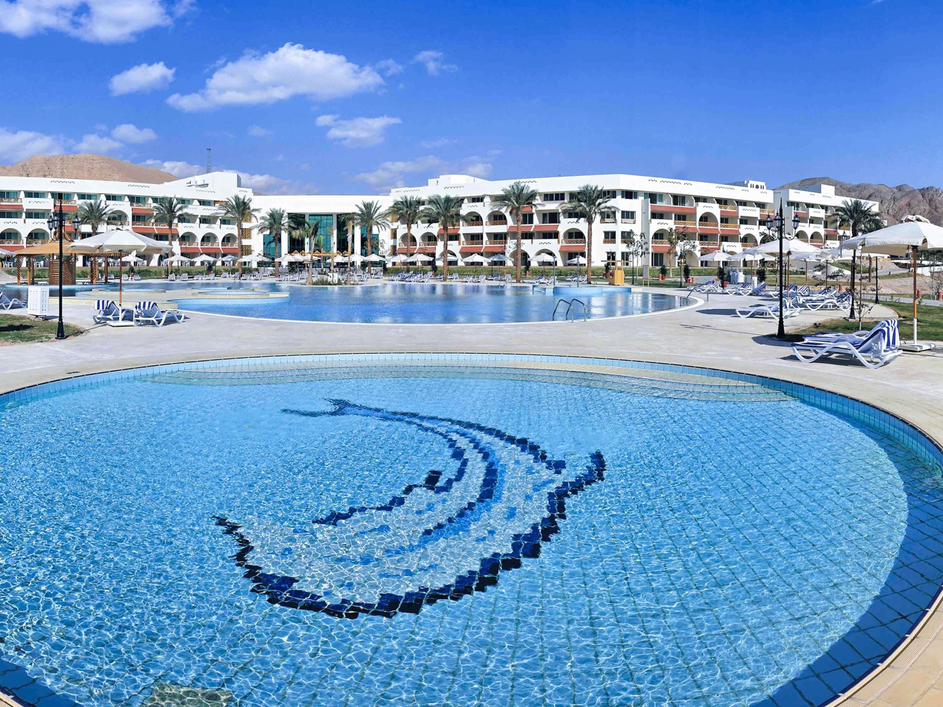 Un hotel con diverse piscine, lettini prendisole e un cielo azzurro limpido.