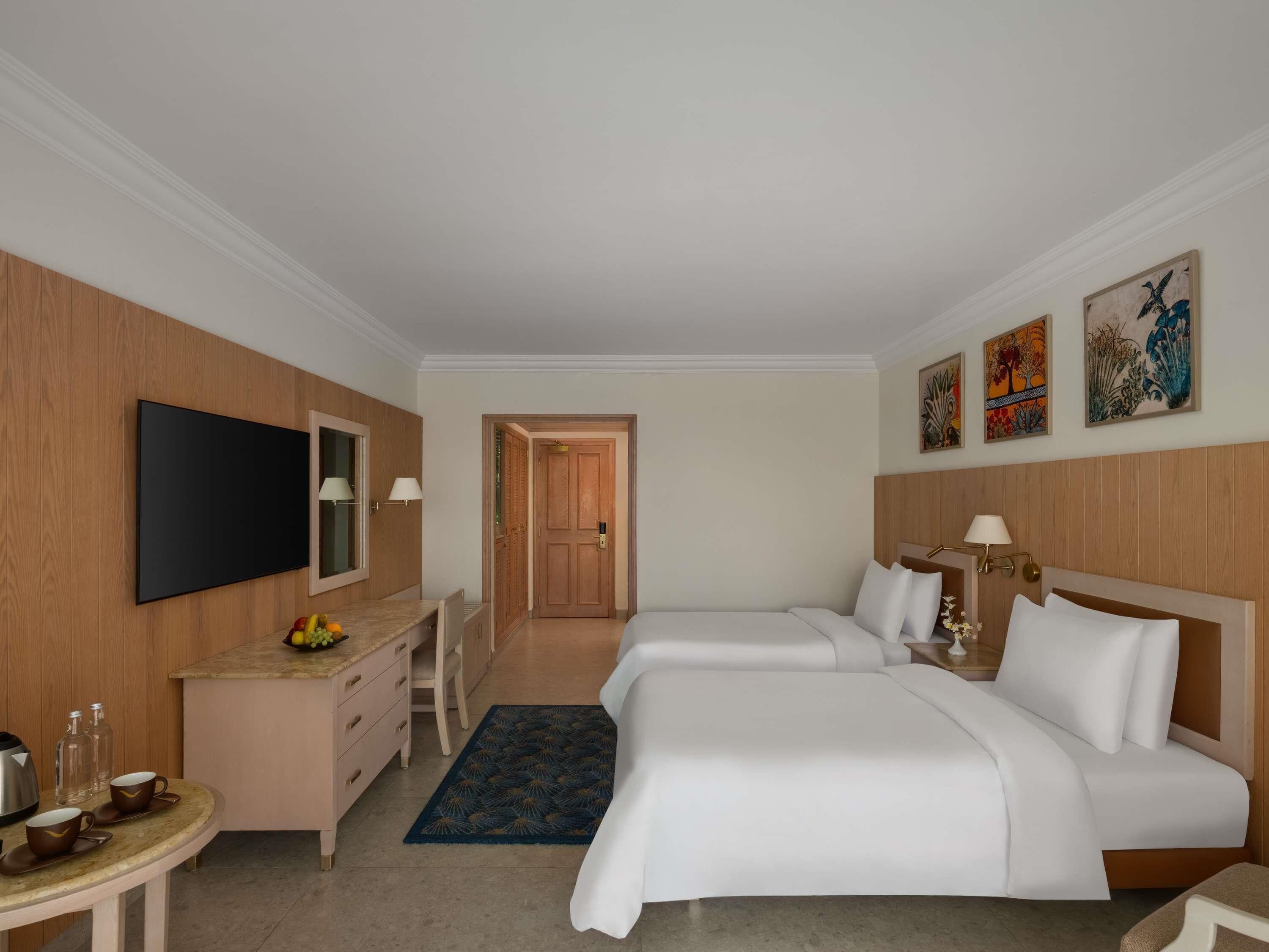 A hotel room with a bed, bedside table, TV, and artwork on the wall.