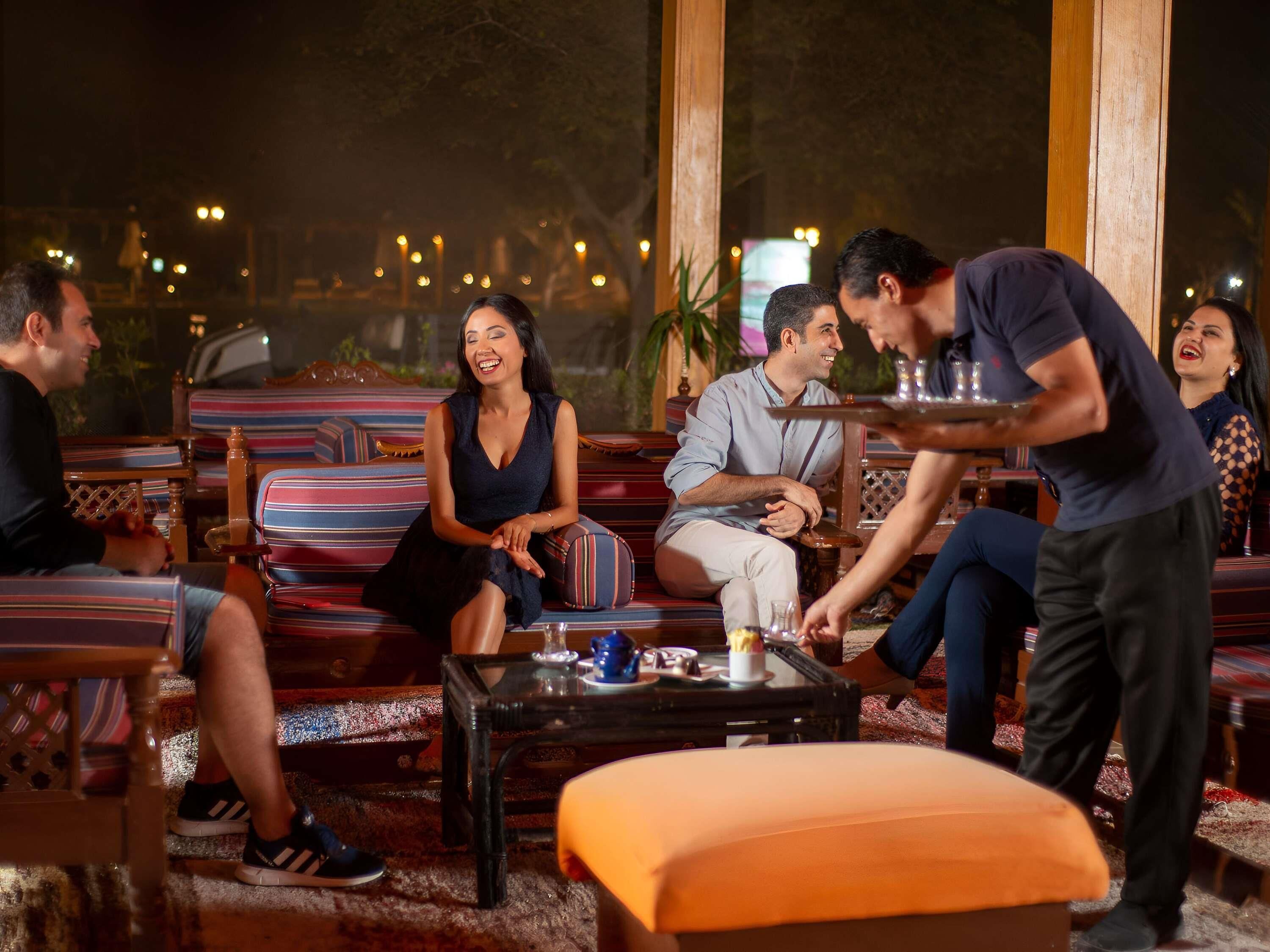 A group of people seated on striped sofas in a well-lit indoor setting with large windows.
