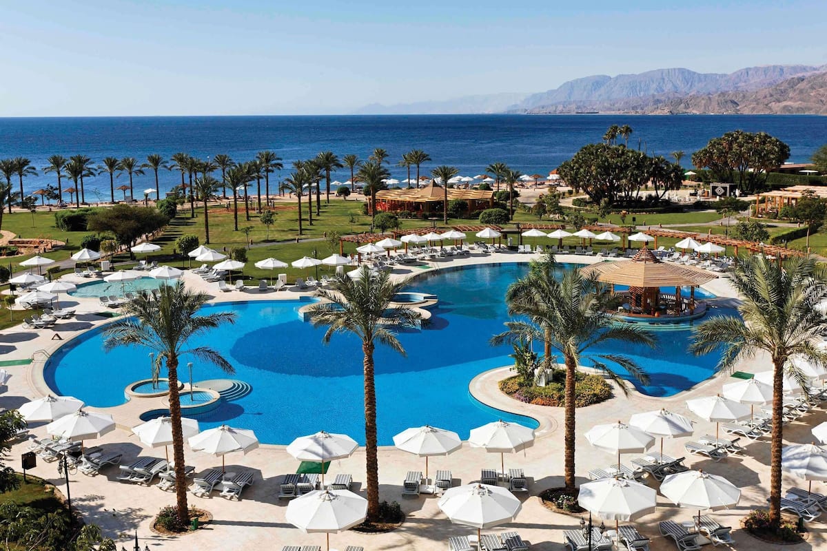 A resort with a large central pool, multiple smaller pools, and a beach area with umbrellas and lounge chairs.