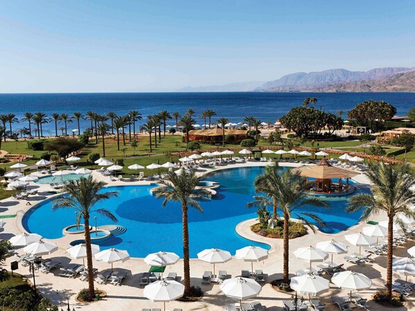 Un resort con una amplia piscina central, tumbonas, sombrillas y vistas al mar.
