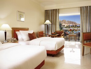 Habitación de hotel con dos camas, zona de comedor con mesa y sillas, y vista a las montañas desde la ventana.