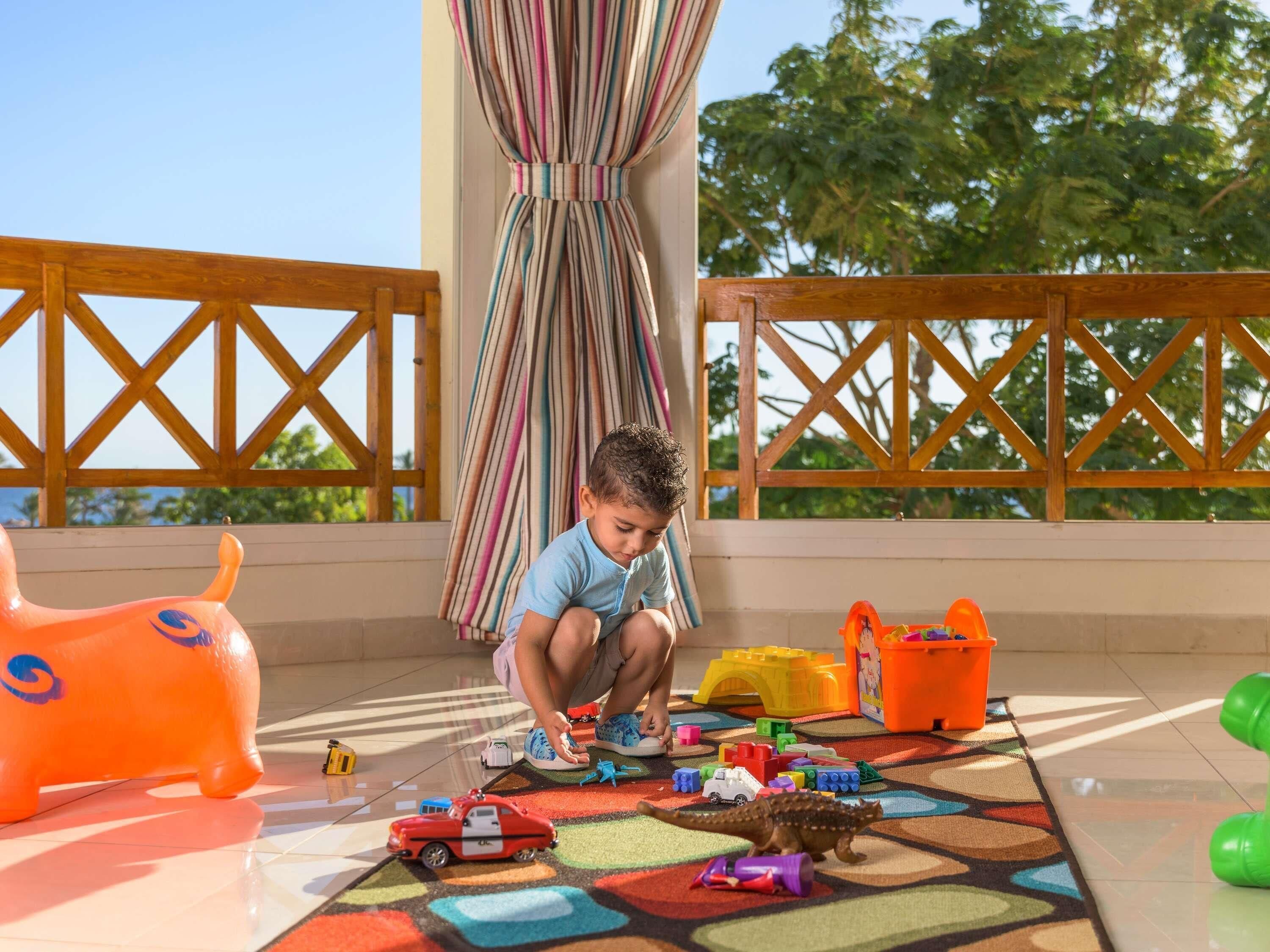 Niño jugando con juguetes en un balcón con vistas a árboles.