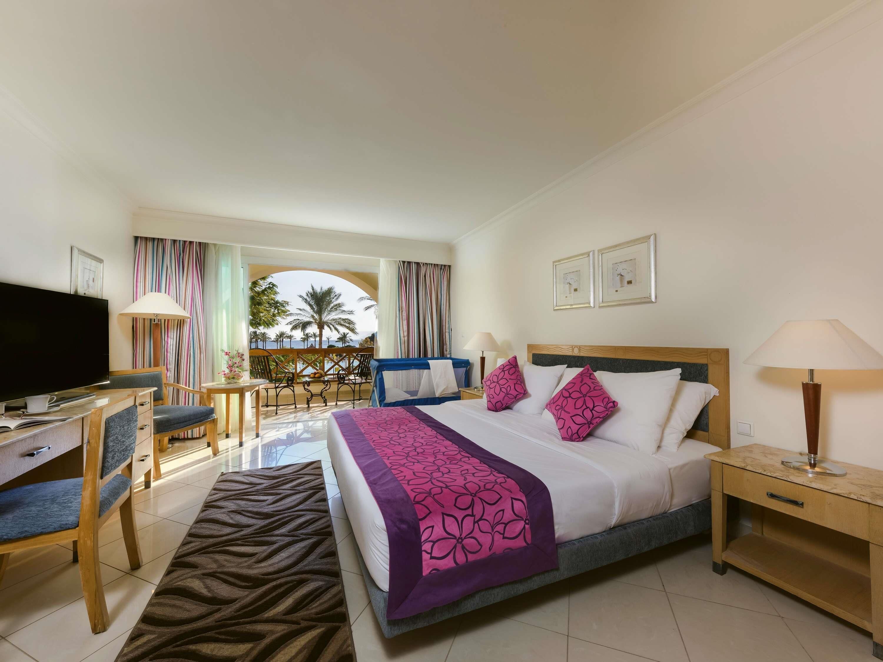 A hotel room with a bed, desk, TV, and balcony with a view.