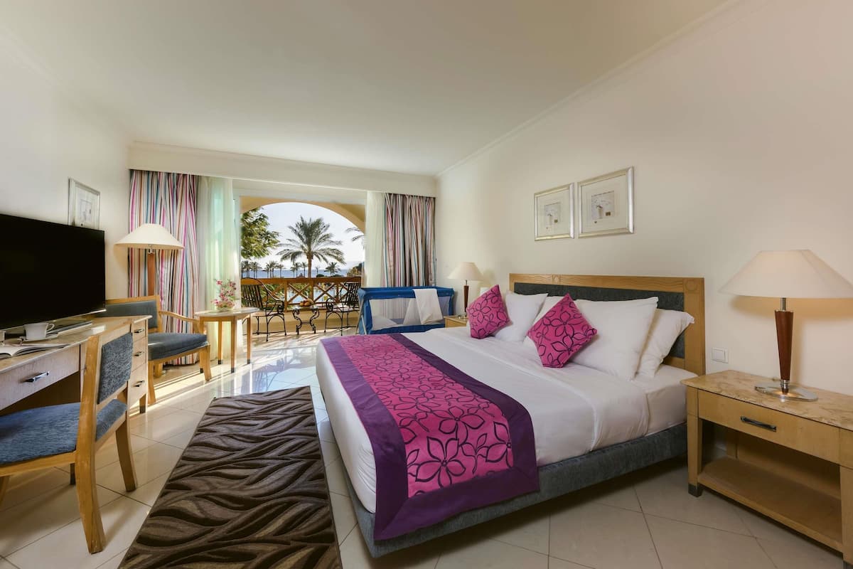 A hotel room with a bed, desk, TV, and balcony with a view.