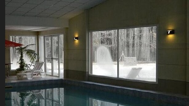 Una piscina interior con paredes de vidrio transparente, un área de descanso con sillones y vistas a un paisaje nevado a través de amplios ventanales.