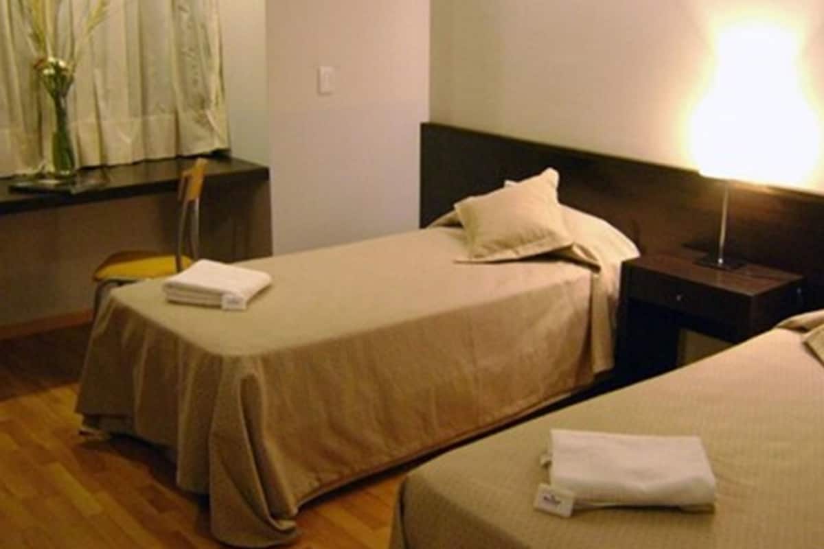 Une chambre d’hôtel avec deux lits simples, une table de chevet, une lampe et une fenêtre avec des rideaux.