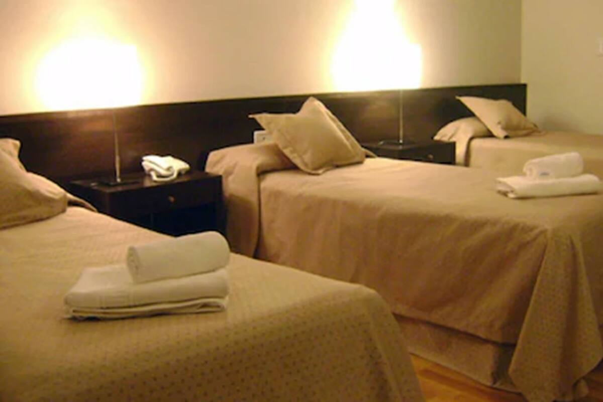 Une chambre d’hôtel avec deux lits simples, chacun muni d’un oreiller et d’une serviette pliée. On y trouve une table de chevet avec un téléphone et une lampe.