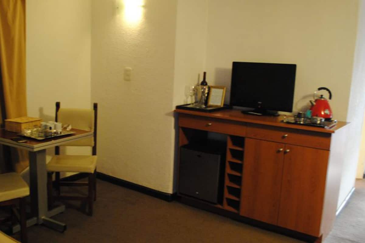 Une chambre d’hôtel de taille réduite, comprenant un lit simple, un petit bureau avec une chaise, une télévision et un mini-bar.