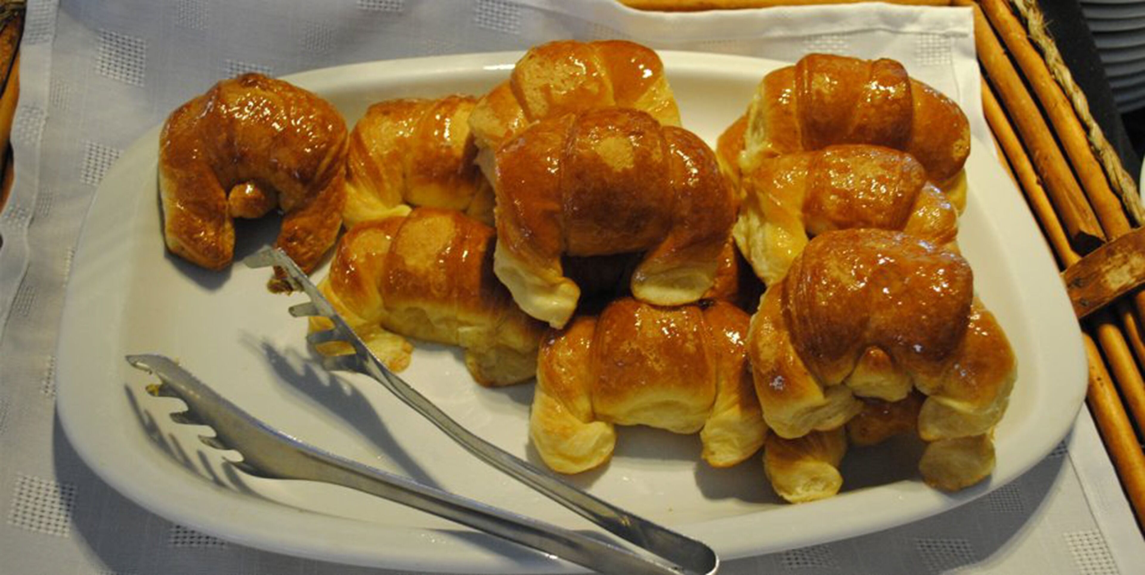 A plate of glazed croissants on a white plate with a fork and knife beside it.