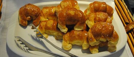 A plate of glazed croissants on a white plate with a fork and knife beside it.