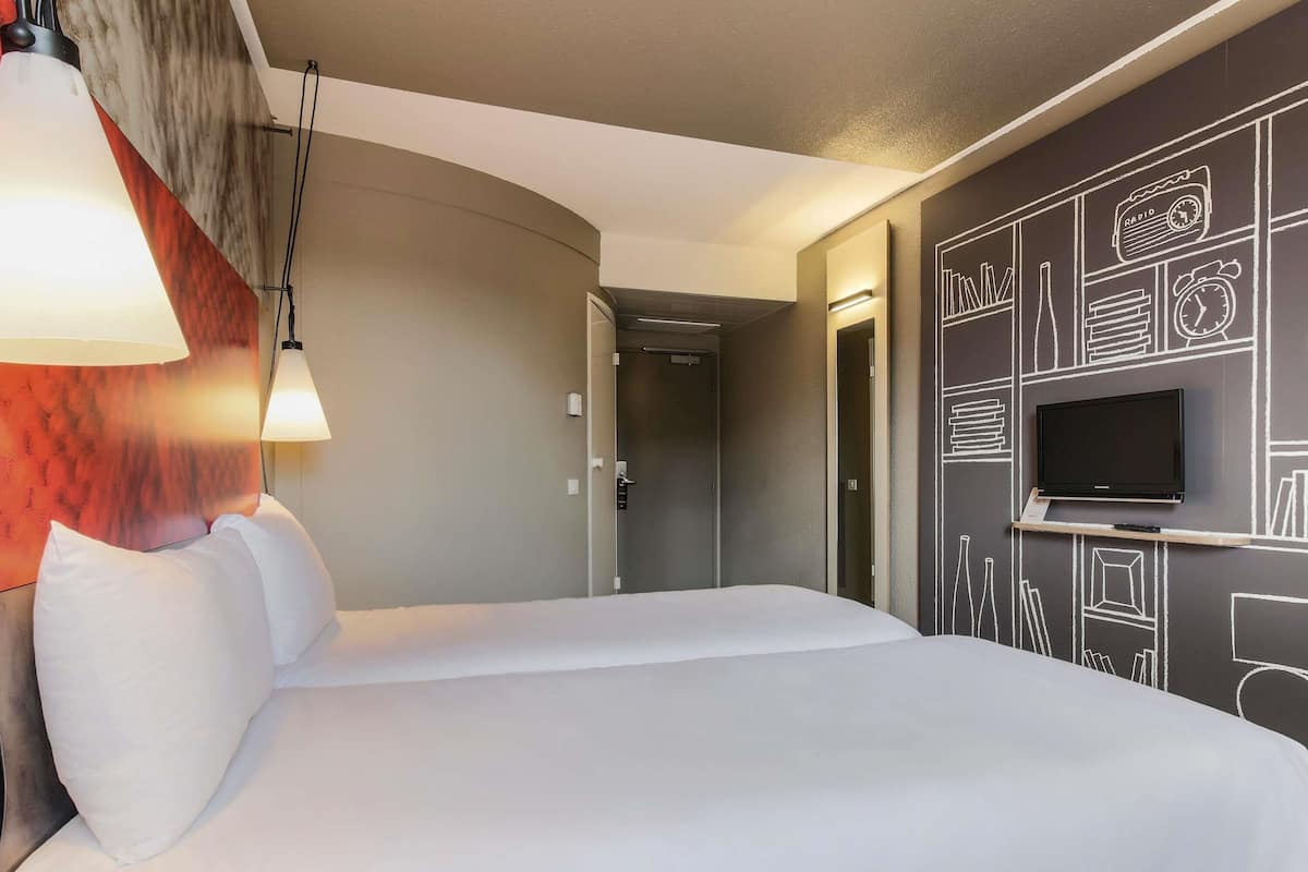 A hotel room with a bed, a TV mounted on the wall, and a lamp.