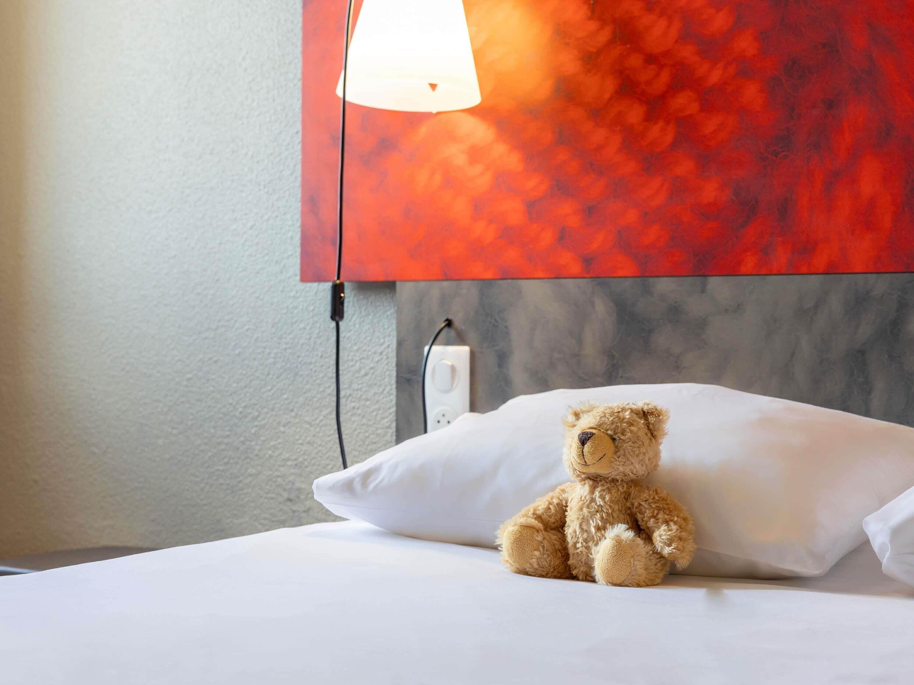 A bed with a white pillow and a teddy bear sitting on it.