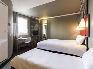 A hotel room with two beds, a desk with a chair, a television, and a window with curtains.