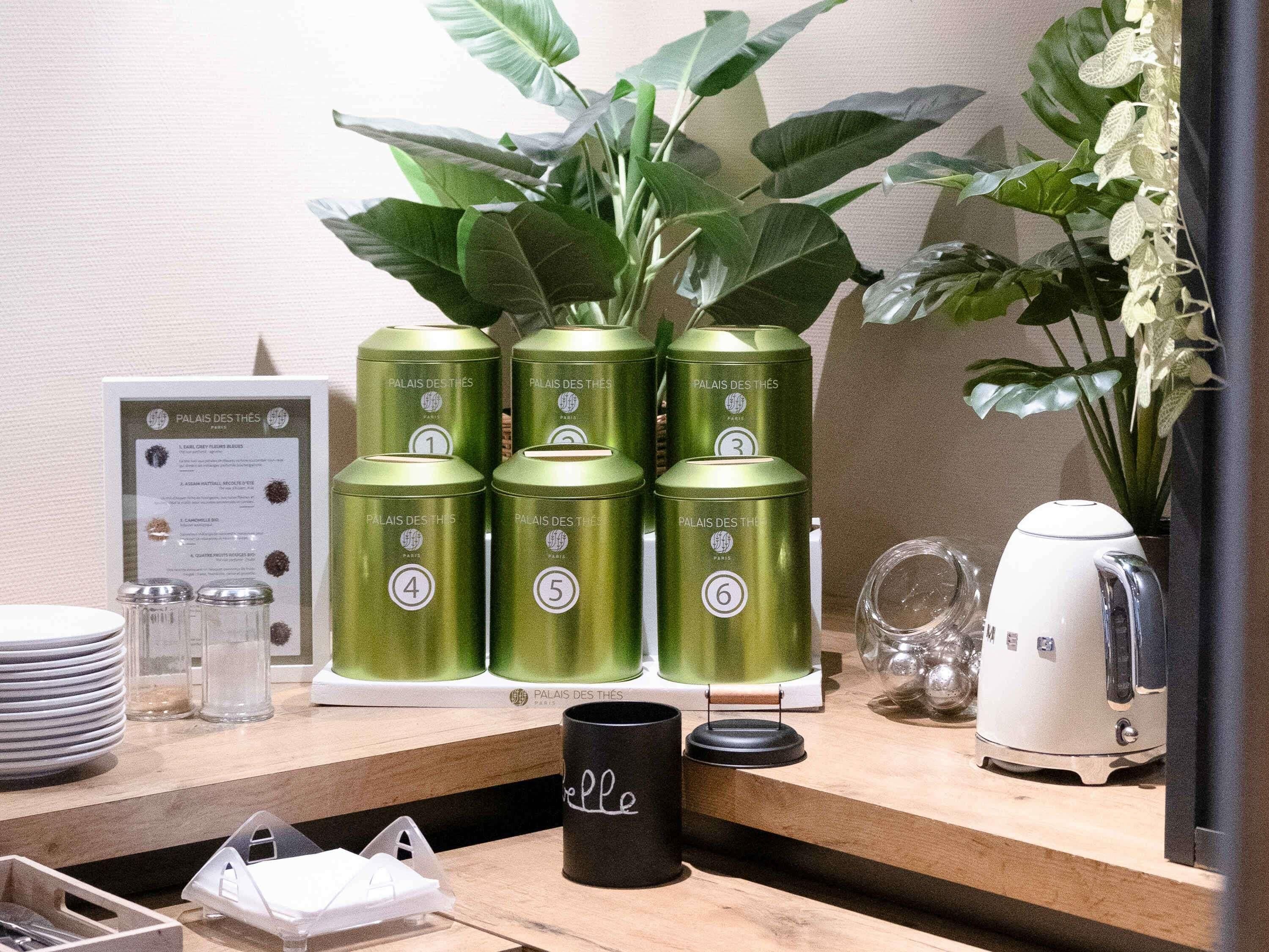 A kitchen counter with green canisters, a black mug, a coffee maker, and a framed menu.