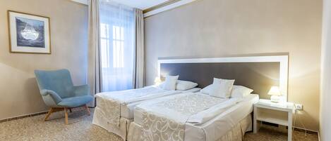 A hotel room with a large bed, a chair, a nightstand, and a chandelier.