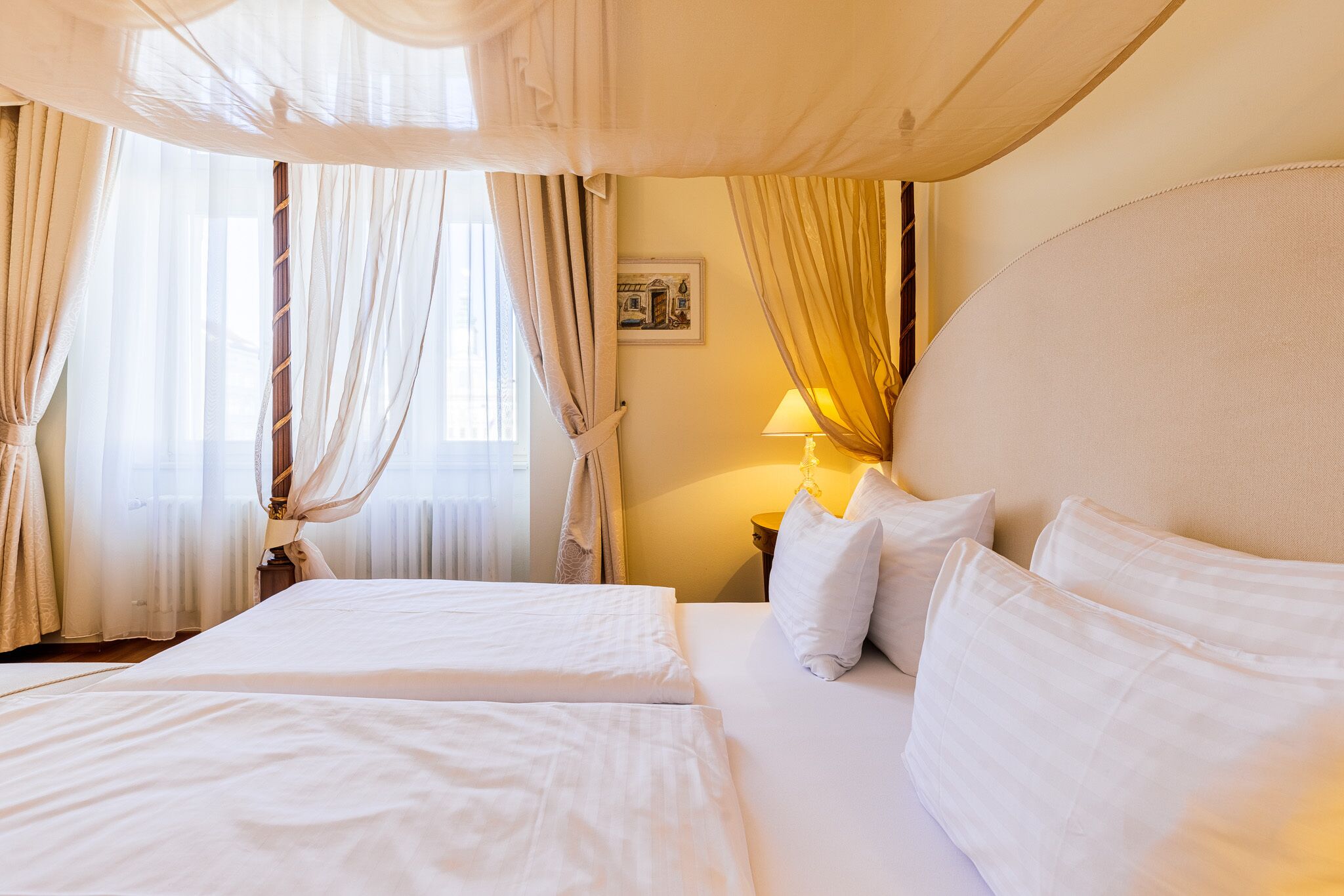 A hotel room with two beds, a nightstand, a lamp, and a window with curtains.