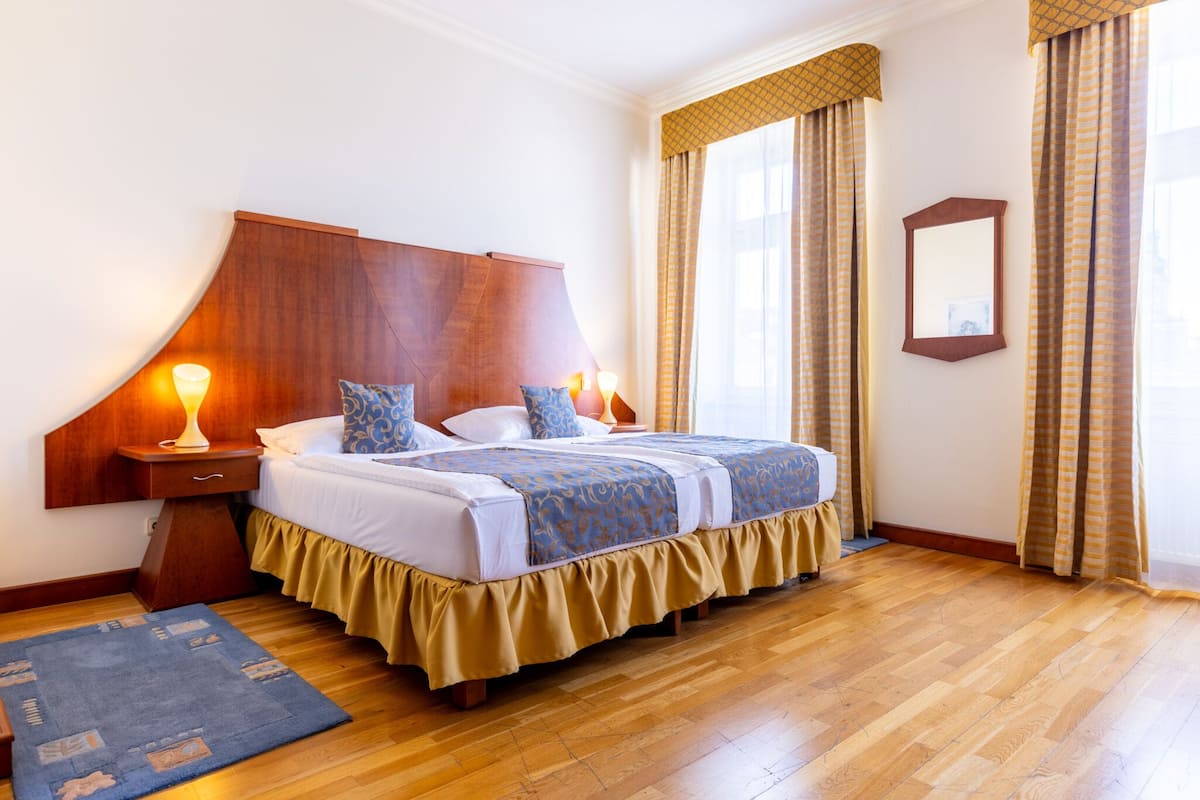 Una cama doble con cabecera de madera, dos lámparas de noche y una colcha de color azul y blanco con estampado.