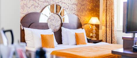 A hotel room with a bed, a round mirror on the headboard, a lamp, and a television.