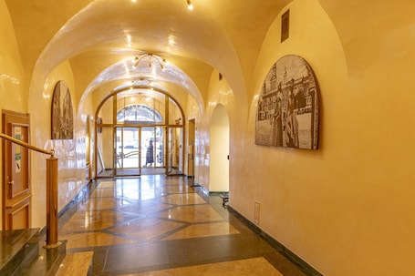 A hotel corridor with a marble floor, arched ceilings, and a large framed picture on the wall.
