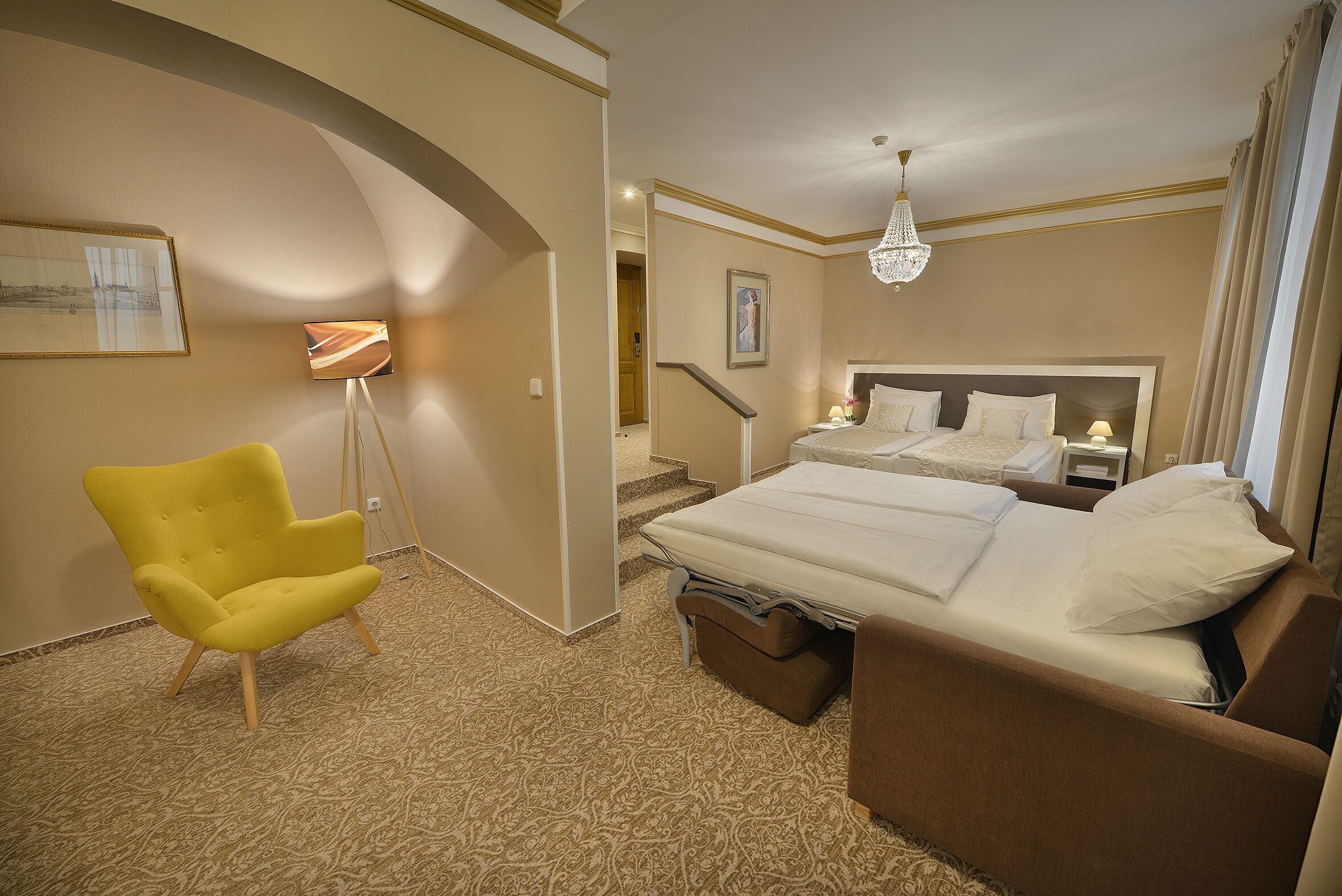 A hotel room with a large bed, a chair, a desk, and a chandelier.