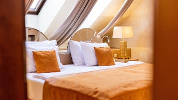 Un dormitorio con tragaluces, una cama con ropa blanca y almohadas anaranjadas, una mesita de noche con lámpara y un cabecero de madera.