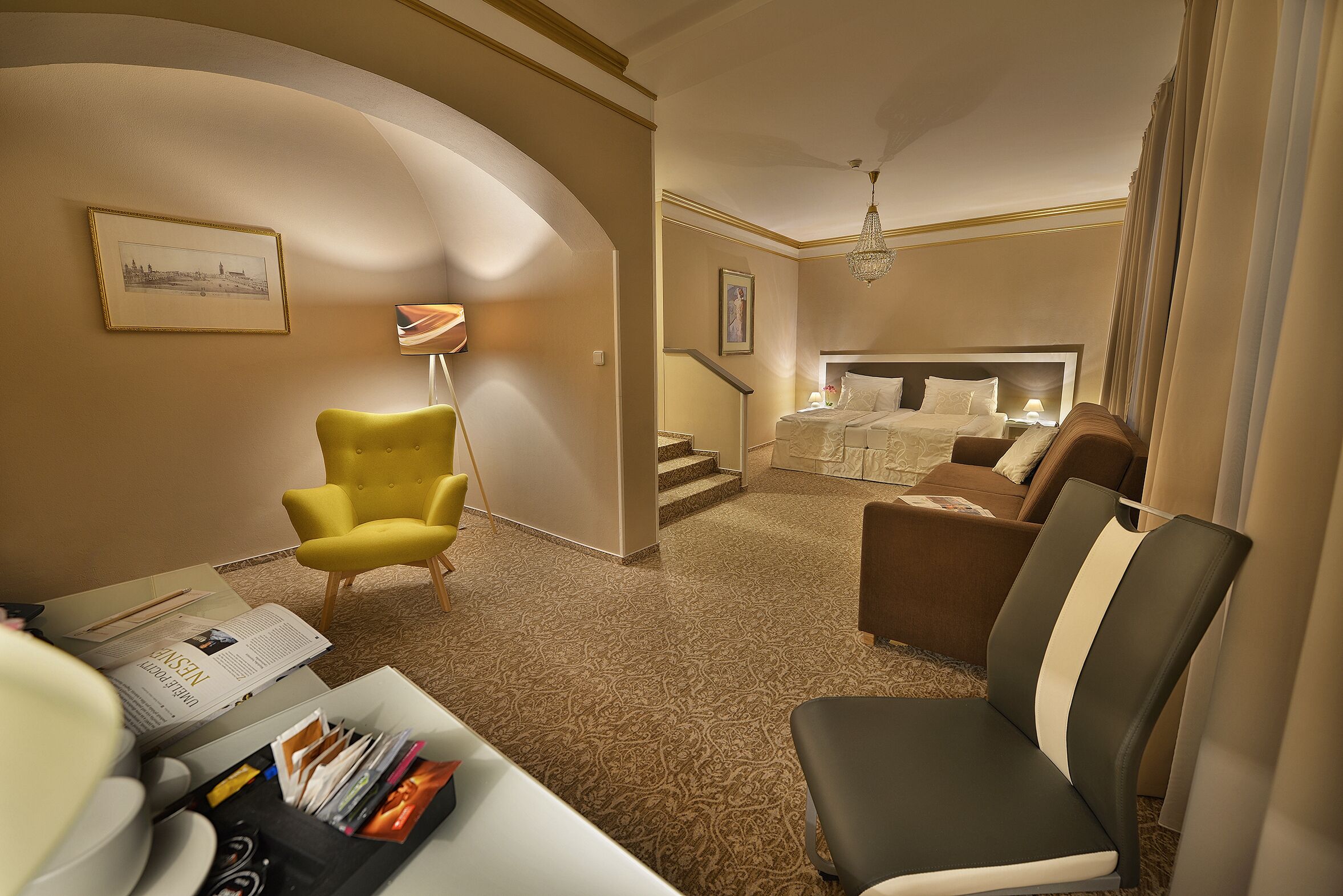 Una habitación de hotel con una pared curva, una cama, un sofá, una silla y un escritorio con una lámpara y algunos libros.