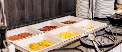 A buffet with various food options including bacon, eggs, and other breakfast items.