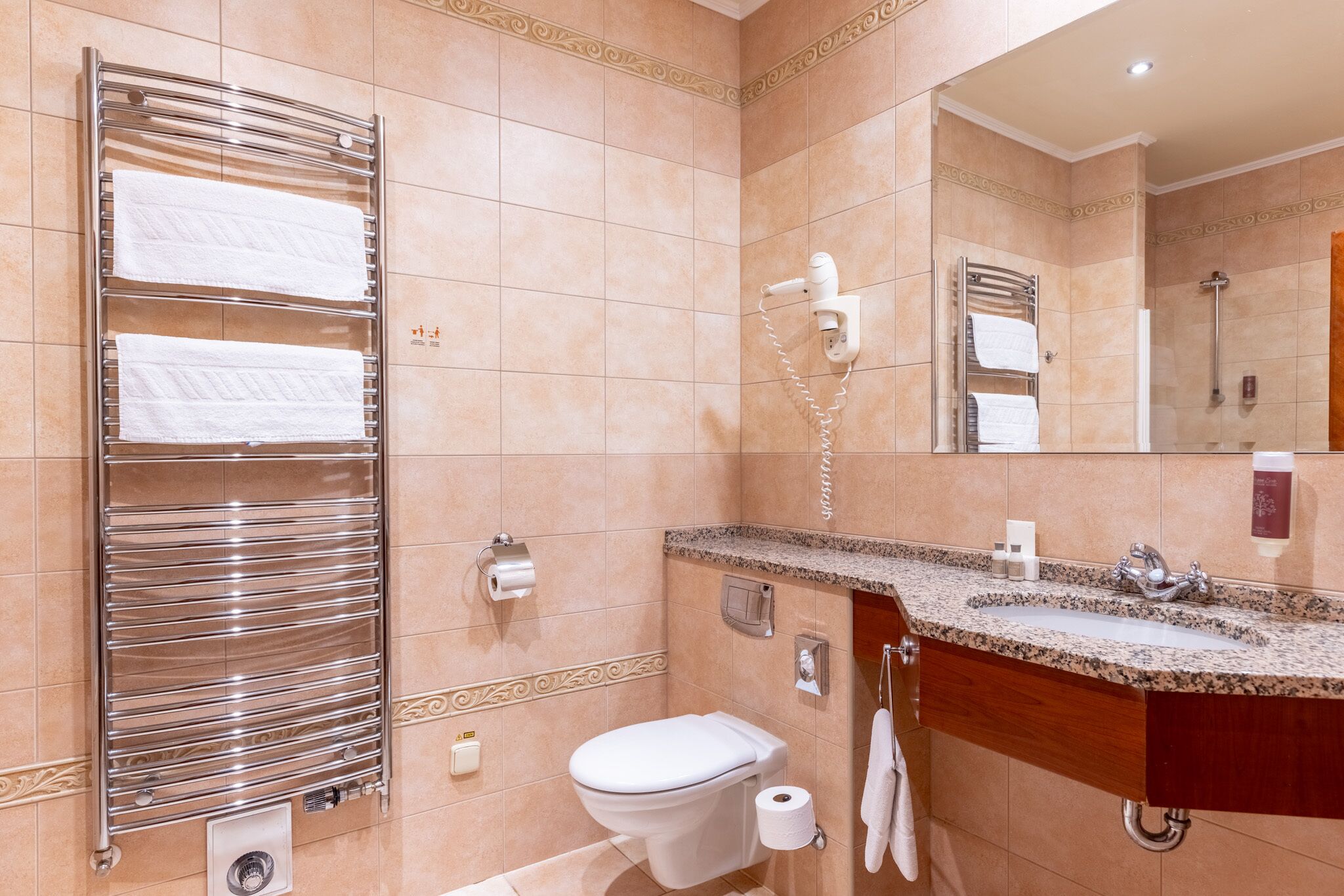 Un baño con ducha, inodoro, lavabo de encimera de granito y toallero con varias toallas.