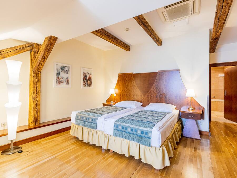 Quarto com teto de madeira, cama com colcha estampada, duas luminárias de cabeceira e mesa de cabeceira de madeira.