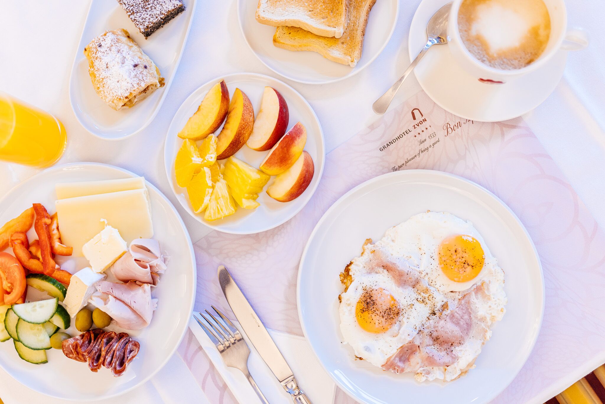 A breakfast setting with plates of eggs, toast, fruit, and cheese.