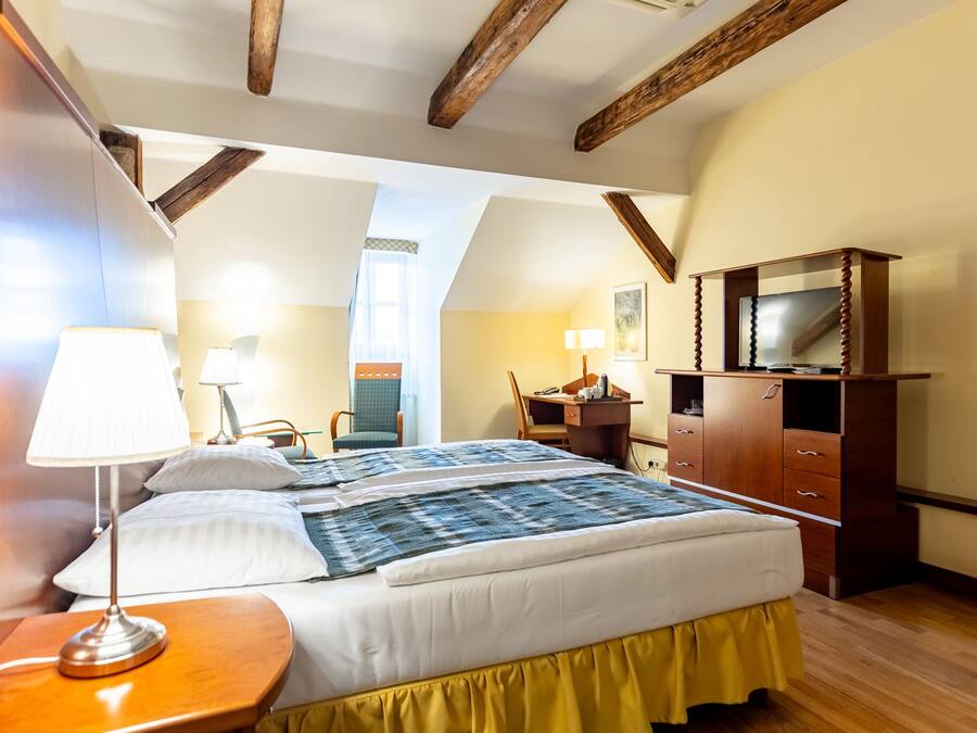 A bedroom with a bed, bedside lamps, a desk, and a television.