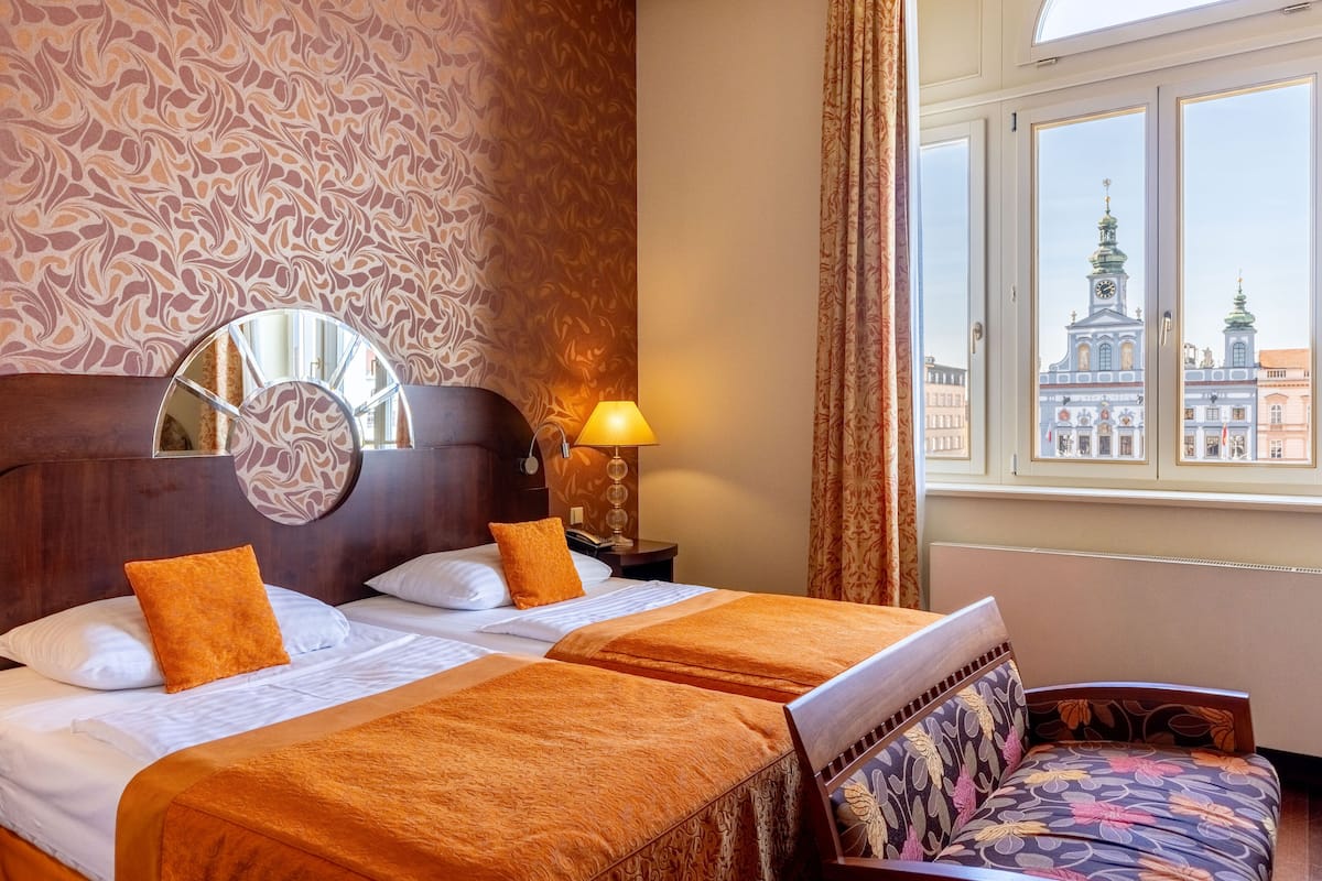 Una habitación de hotel con una cama grande, una mesita de noche, una lámpara, una silla y un ventanal con vistas a un edificio.